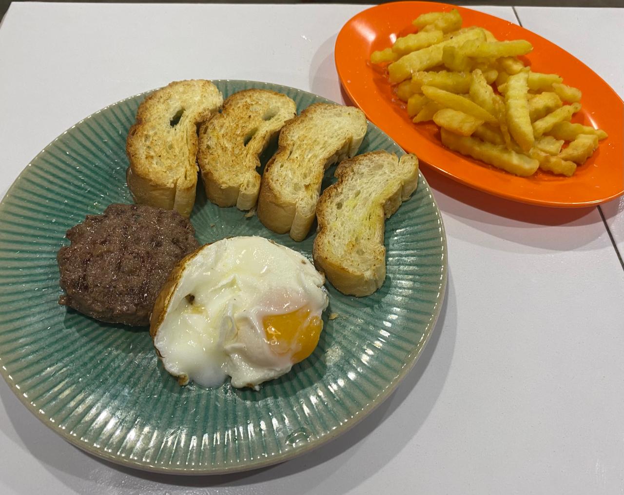 Beef patty with fried egg, toasted bread and fries